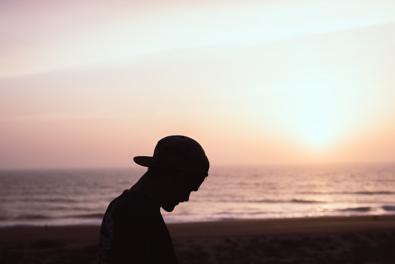 man with cap standing on beach during sunset
