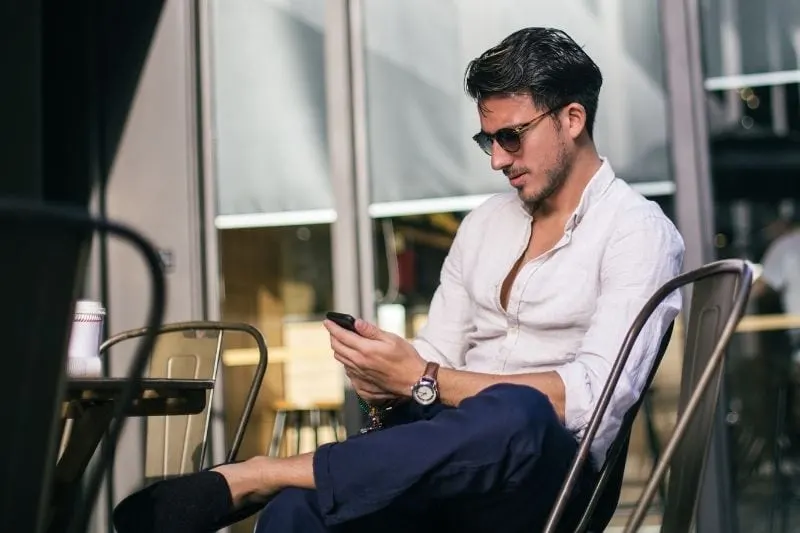 man texting in a cafe wearing sunnies outdoors
