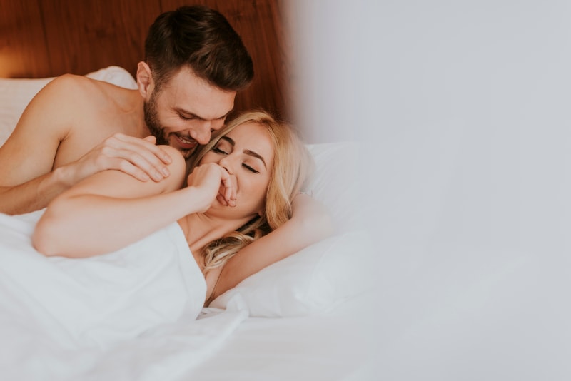 man touching woman's arm while lying on bed