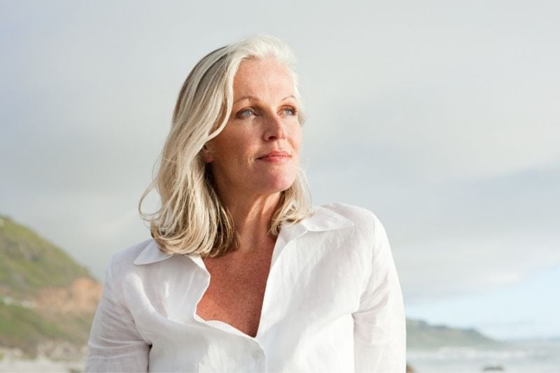 mujer madura en la costa pensando profundamente vestido con top blanco