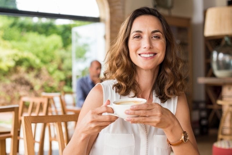 mujer madura en la cafetería tomando café y sonriendo a la cámara