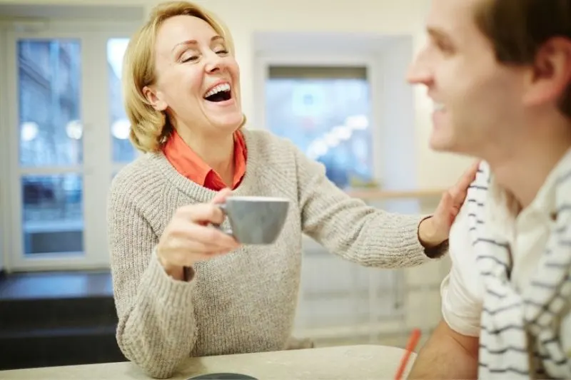 mature woman with a cup of tea laughing with her younger colleague in a cafe