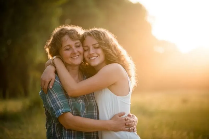 mother and daughter embracing each other in the middle of the field with trees at the background