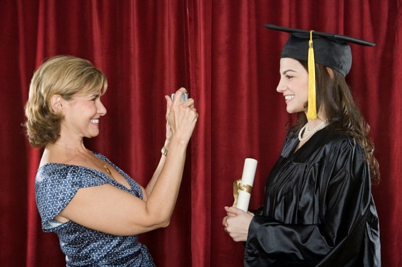 mother taking a picture of her graduating daughter wearing toga in the stage