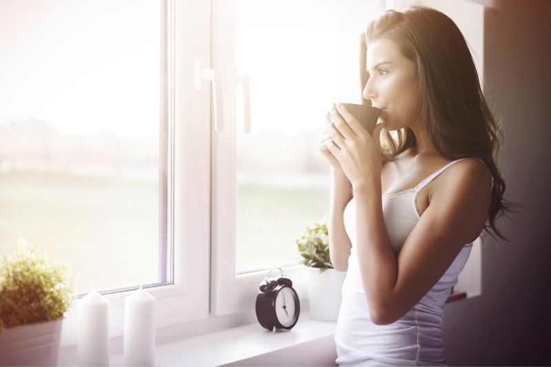 donna pensierosa che beve il caffè al mattino con indosso un indumento intimo bianco