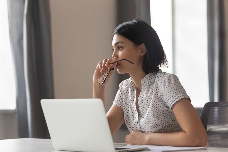 Donna pensierosa in ufficio che tiene gli occhiali da vista mentre pensa al tavolo dell'ufficio