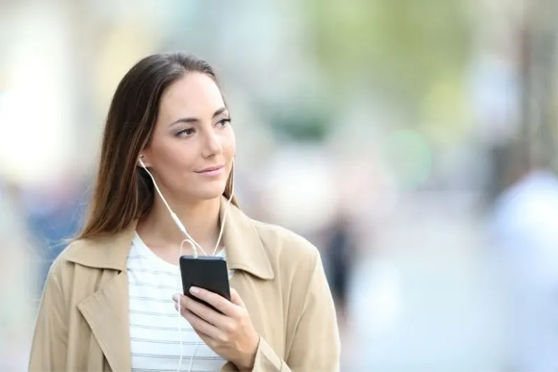 pensive woman listening to music from her smartphone while walking outside