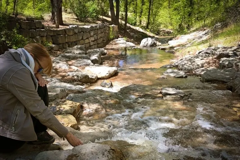 pensive woman near stream touching the water flowing