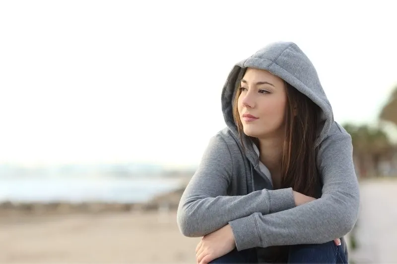 pensive woman on hoodie sitting in the beach during the day