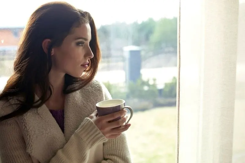 pensive woman sipping coffee early in the morning near the glass window