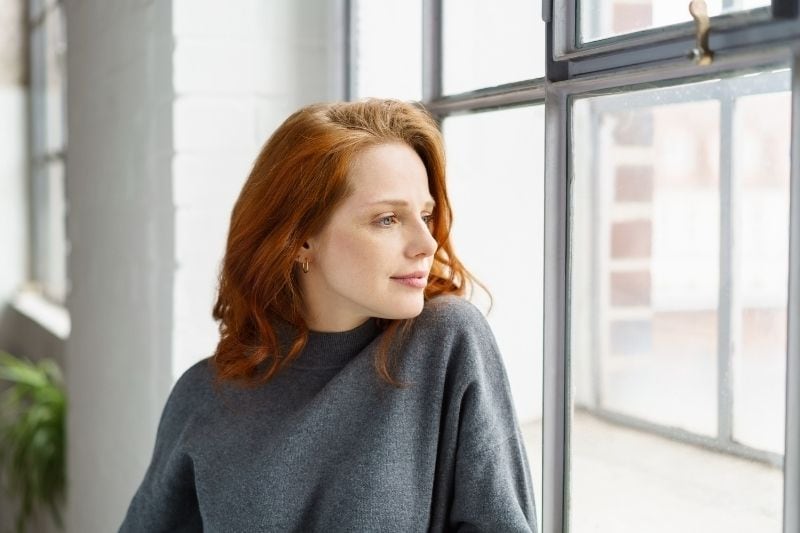 donna pensierosa che sorride vicino alle finestre guardando fuori