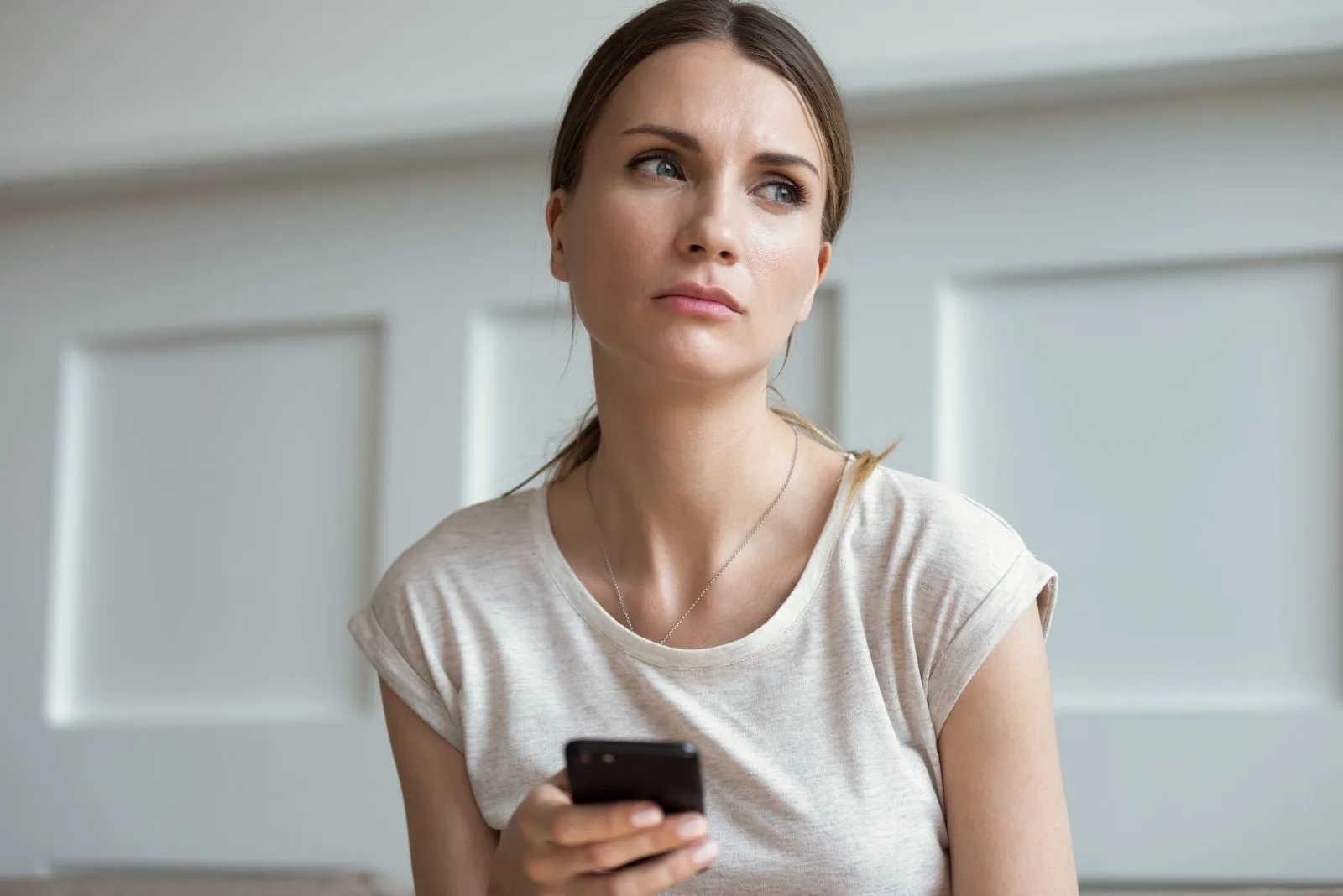 pensive woman texting on smartphone inside home