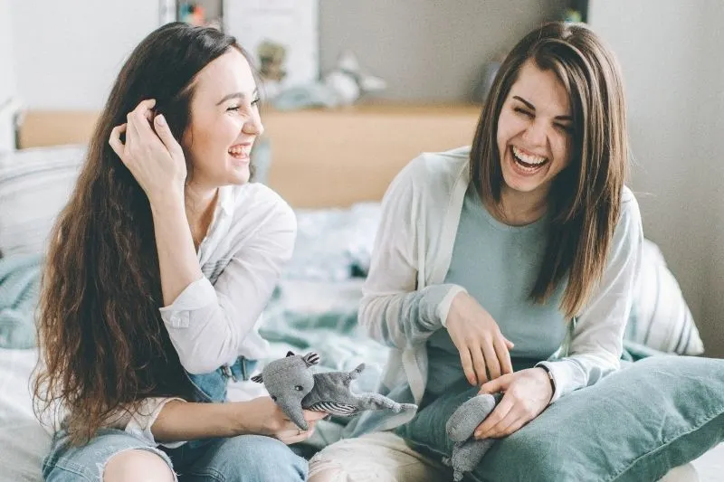 photo of two women laughing and sitting on bed