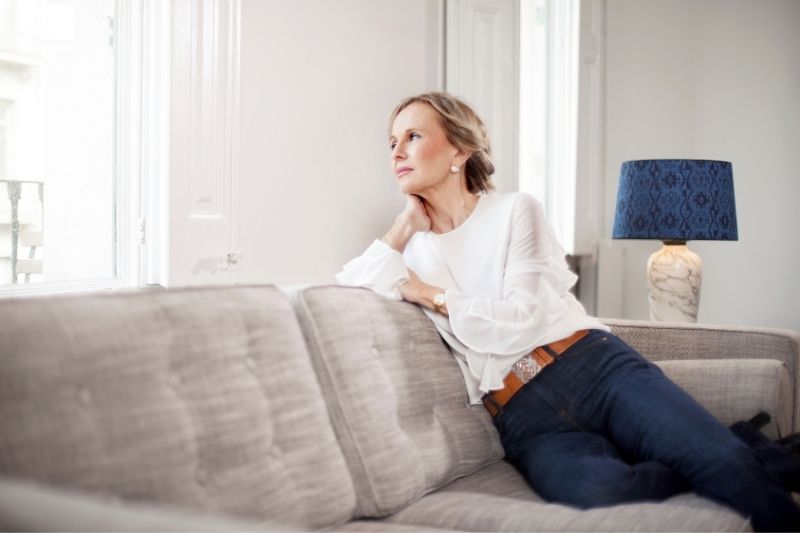 retrato de una mujer pensativa sentada en el sofá mirando por la ventana del salón