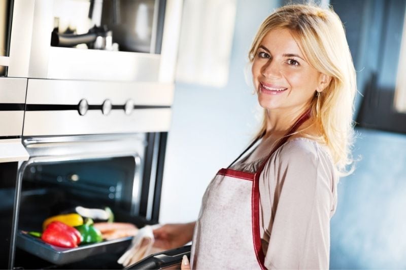 bella donna che cucina e mette il cibo nel forno indossando il grembiule 