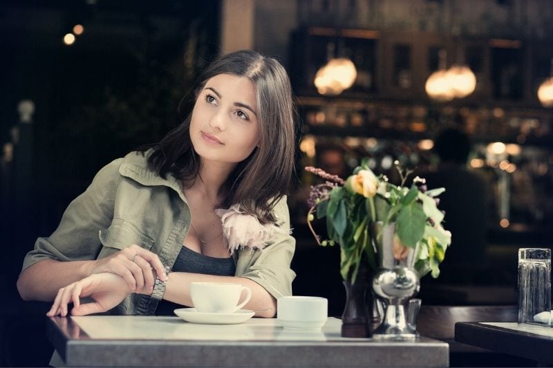 pretty woman waiting for her date at a cafe looking checking her timepiece