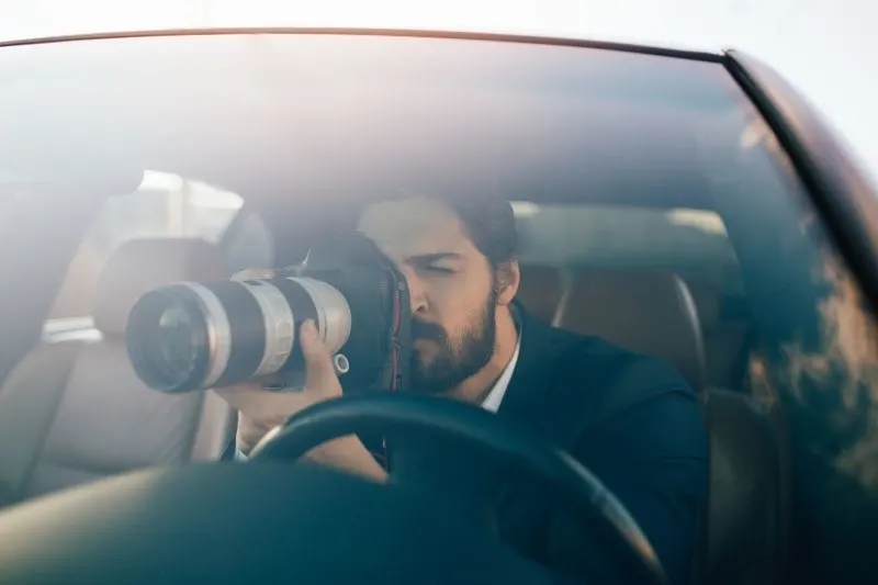 private investigator looking thru the camera while sitting inside the car