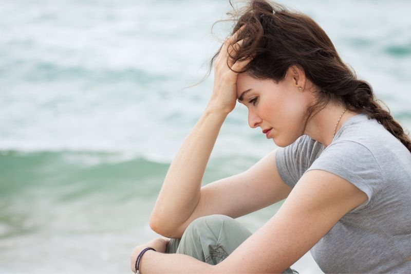 donna triste e depressa seduta a riflettere sulla spiaggia 