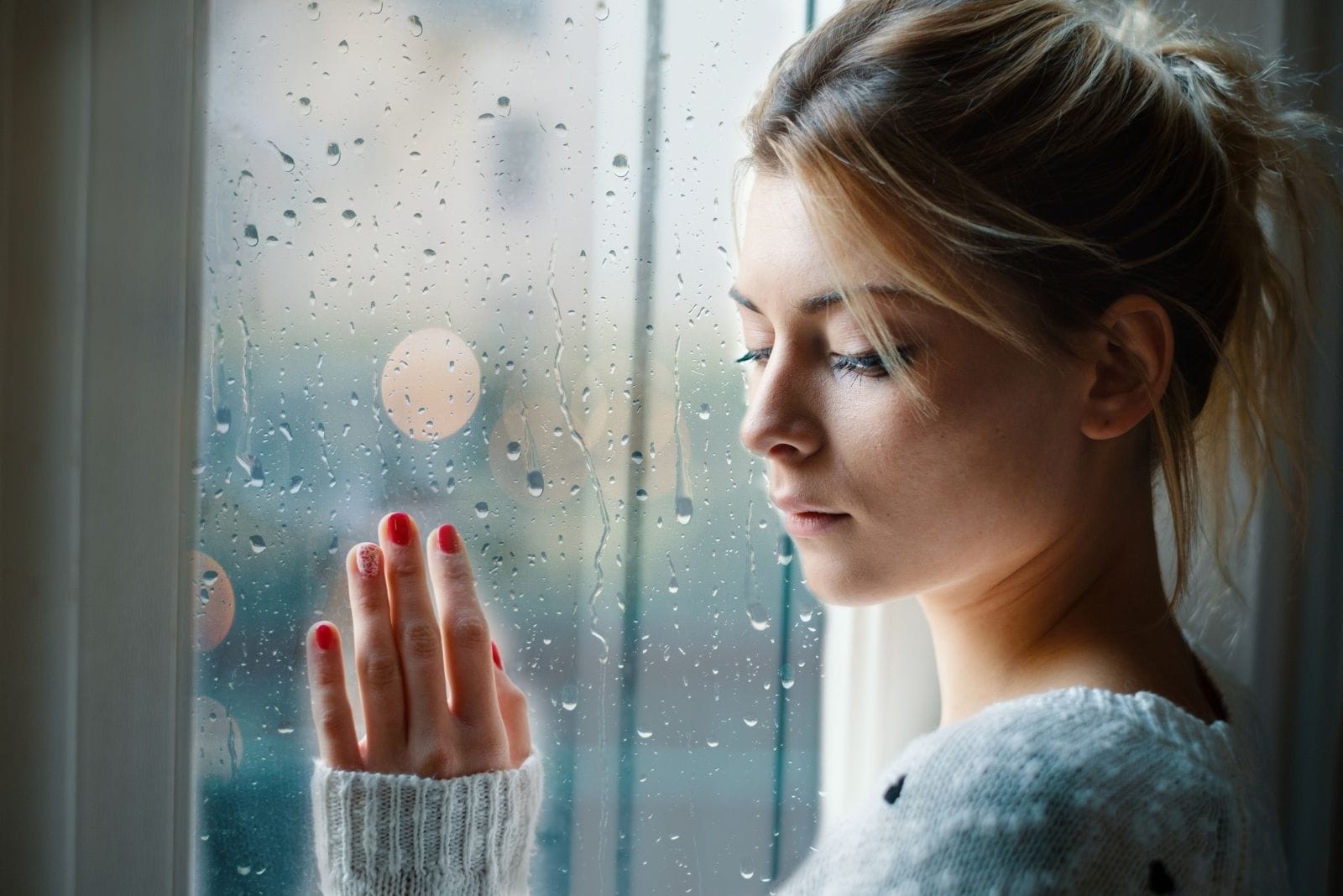 mujer triste tocando las ventanas de cristal con gotas de lluvia 