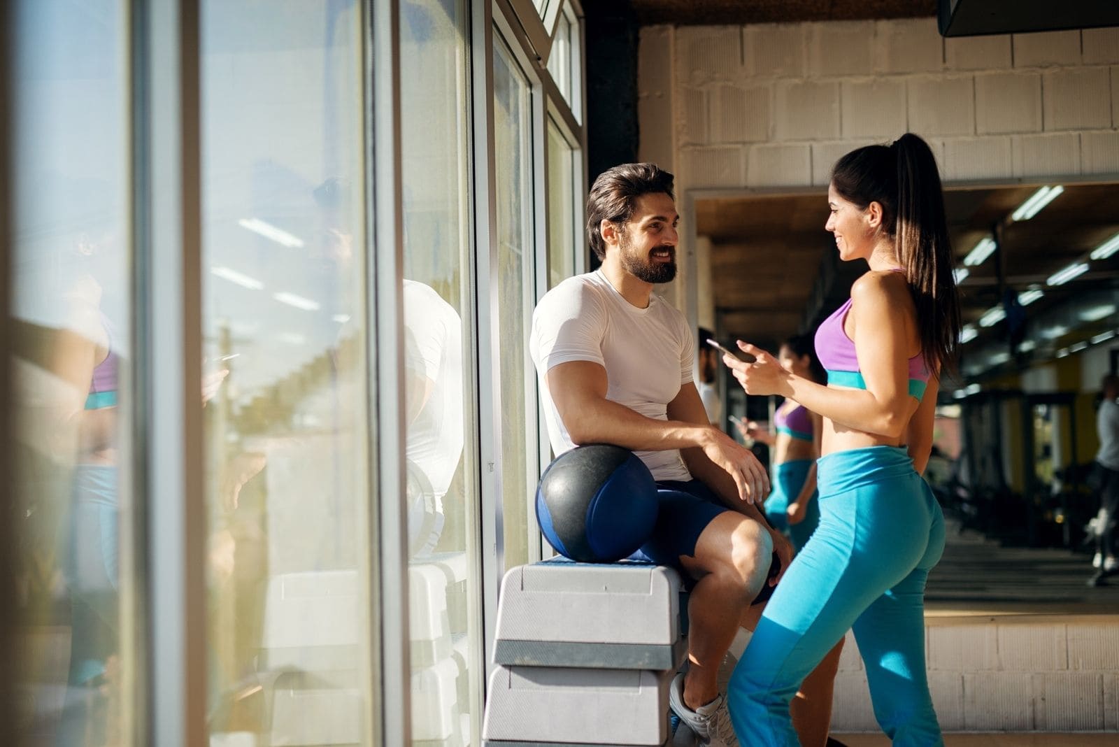 shaped sporty girl flirting with a guy in the gym holding a smartphone