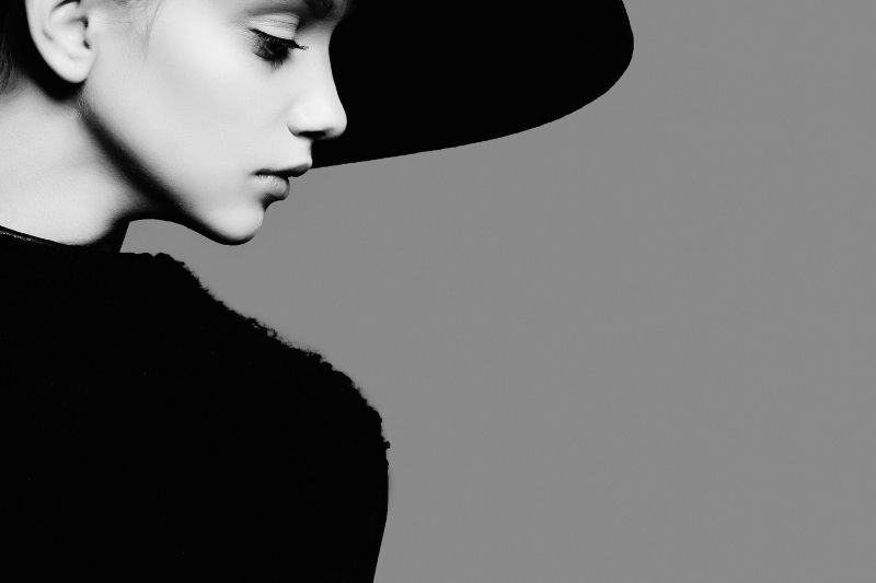 vista laterale di una donna in posa con cappello e abito nero