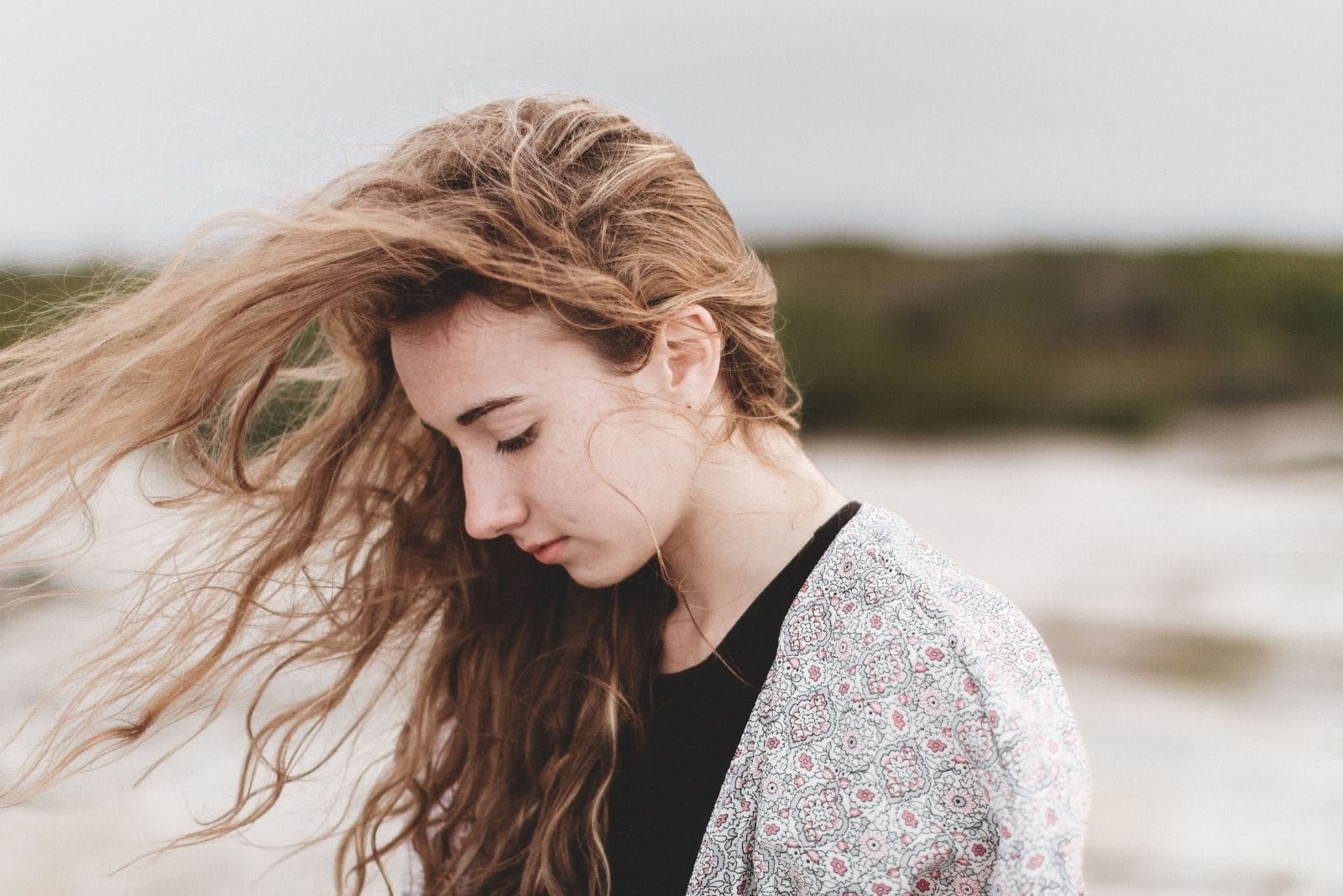 vista laterale di una giovane donna triste e pensierosa con i capelli mossi dal vento che cammina all'aperto