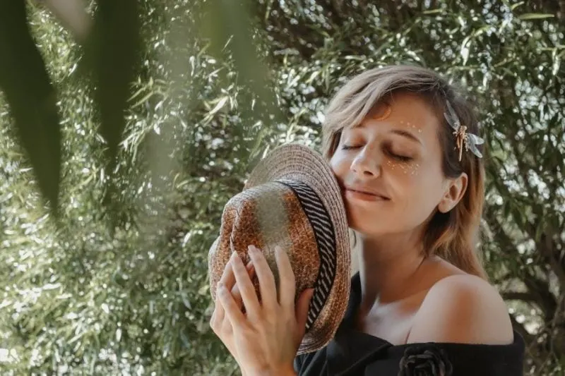 smiling mindful woman in the garden holding a hat with a dragonfly in her head