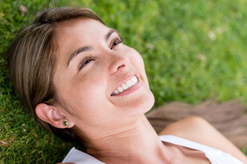 mujer sonriente tumbada en la hierba/el suelo pensativa enfoque en el rostro