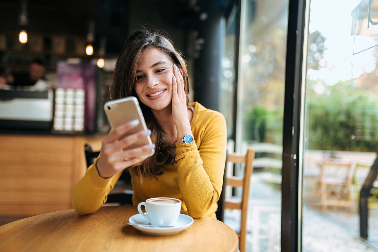 donna sorridente di 20-30 anni che messaggia al cellulare e sorride all'interno di un caffè