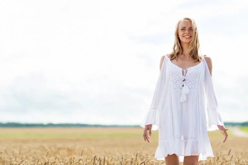 smiling woman standing in the middle of the wheat field wearing white dress