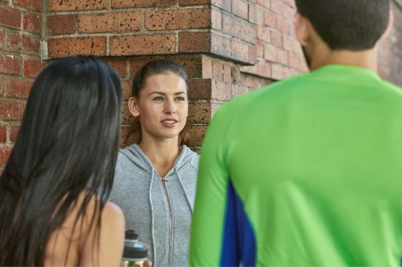 donna sorridente che parla con gli amici dopo un allenamento all'aperto vicino a un muro di mattoni