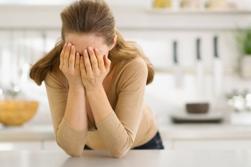 stressed woman in the kitchen covering her face with her hands