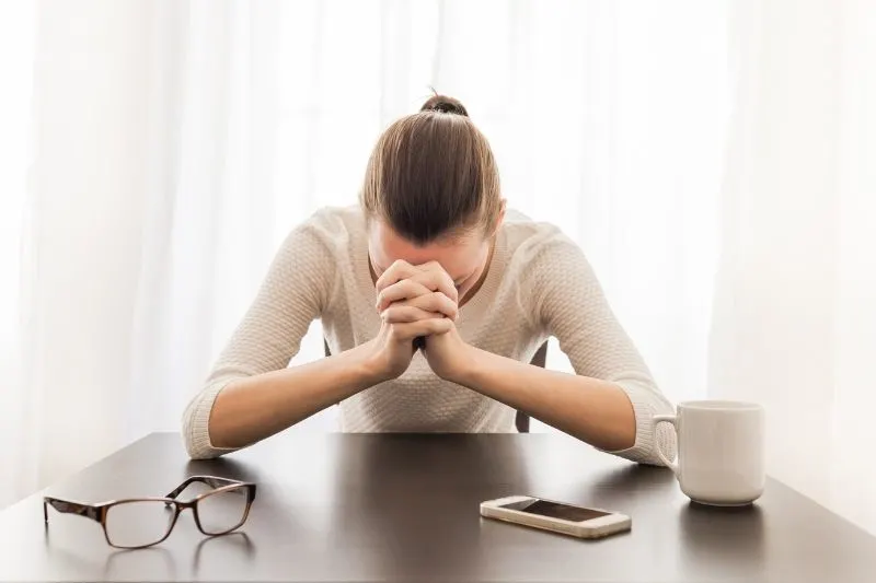 stressed woman in the office setting with close fist and eyeglasses placed on the table