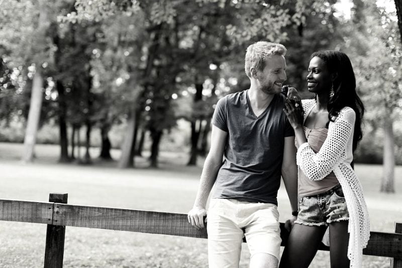 sweet multiracial couple standing and leaning agaings a wooden railing in the park