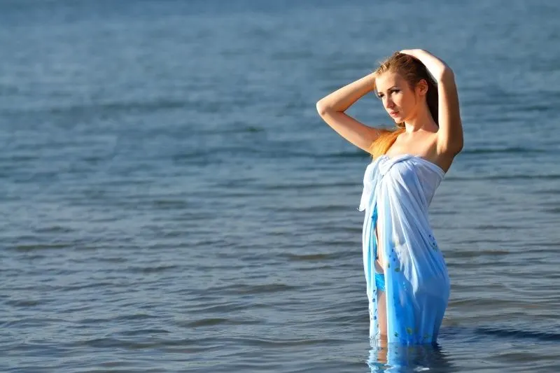 thoughtful woman in the waters with wet cloth covering her and holding her hair