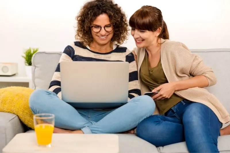 two beautiful women working at home in a laptop sitting in the sofa