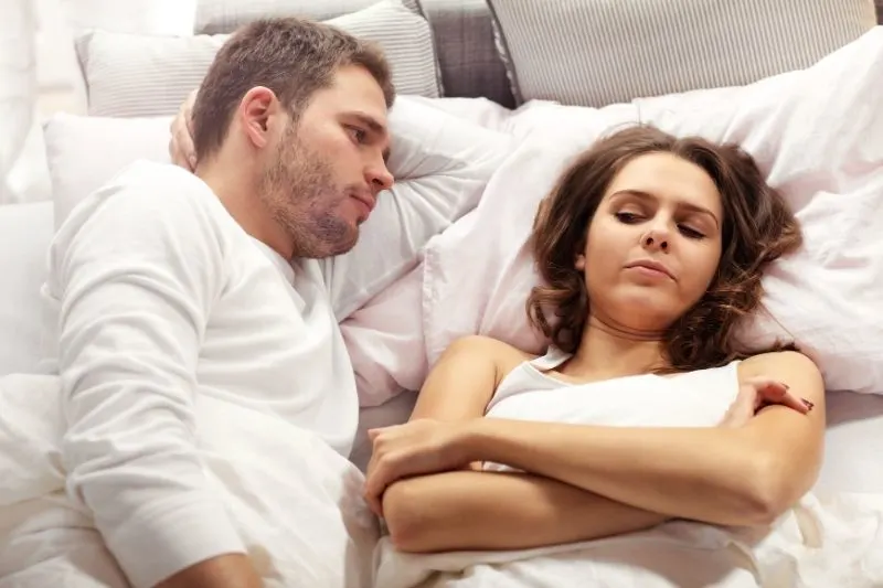 unhappy couple arguing in bed lying down with man facing the woman