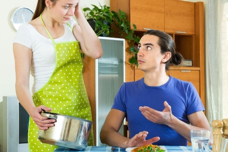 mujer infeliz sirviendo comida marido insatisfecho en la mesa del comedor