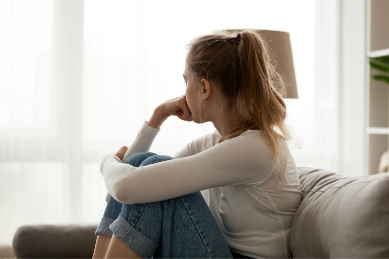 upset blonde woman sitting on couch alone in the living room with feet tucked in