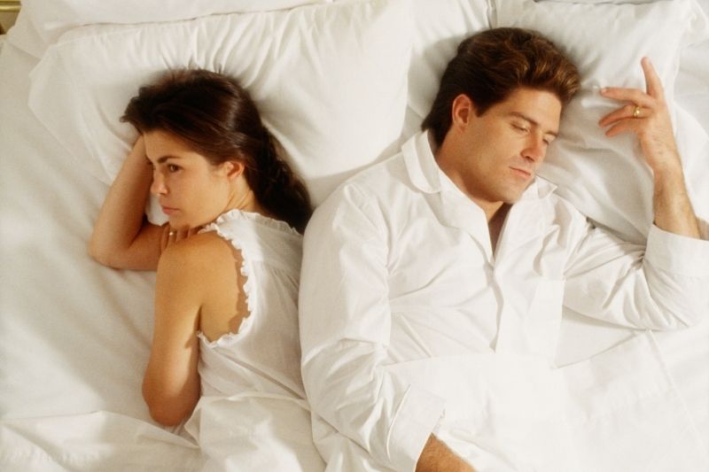 coppia sconvolta a letto, sdraiata in pigiama bianco