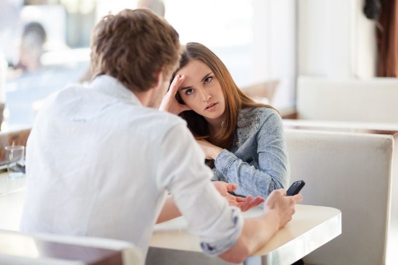 upset woman facing a man holding a phone inside a cafe