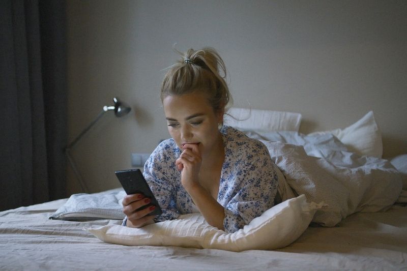 donna che naviga sullo smartphone mentre è sdraiata sul letto durante la notte