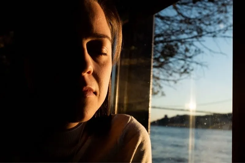 woman closed eyes thinking deeply indoors with house near the body of water