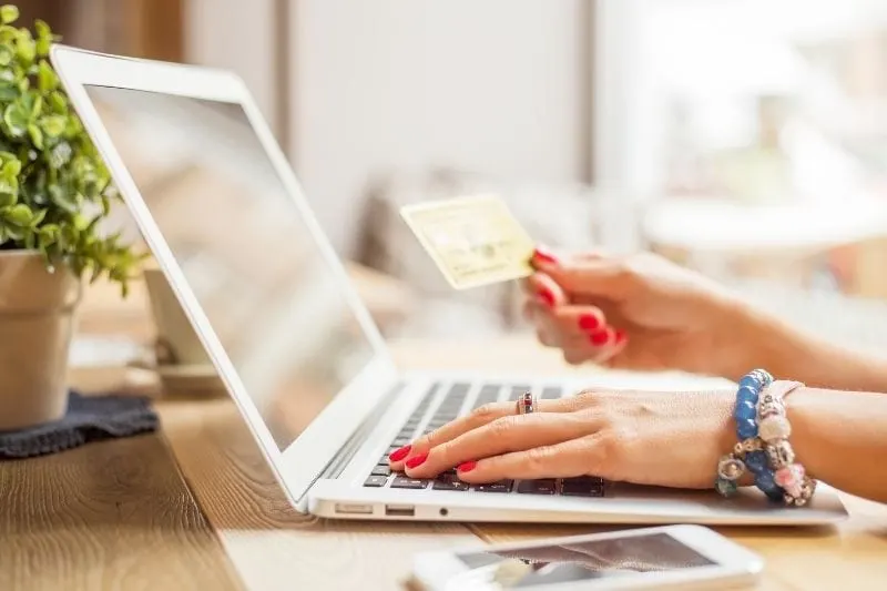 woman holding an atm card while browsing the internet in her laptop
