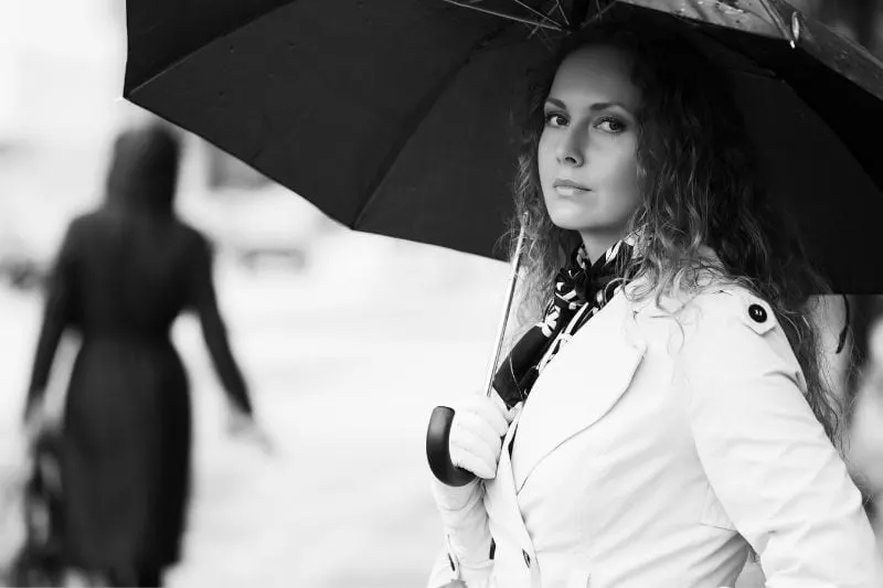 woman holding an umbrella wearing white trench coat in grayscale photography