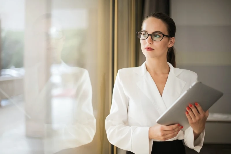 woman in white shirt holding tablet while looking through window