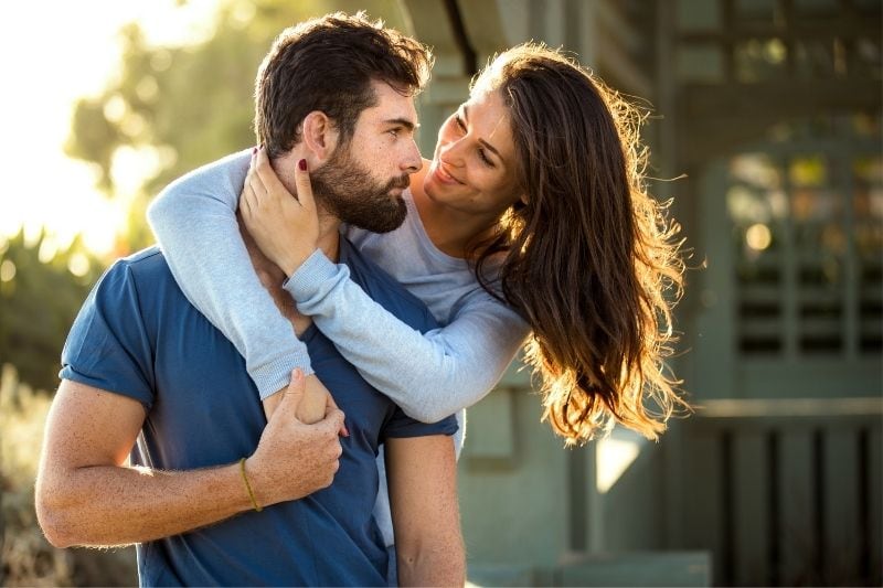 donna che abbraccia una donna mentre l'uomo le rivolge uno sguardo affettuoso in piedi all'aperto