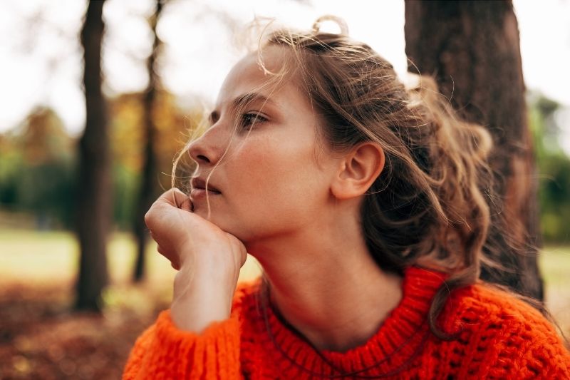 mujer con jersey naranja pensando profundamente sentada al aire libre