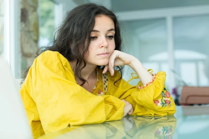 sad woman in yellow shirt leaning on table