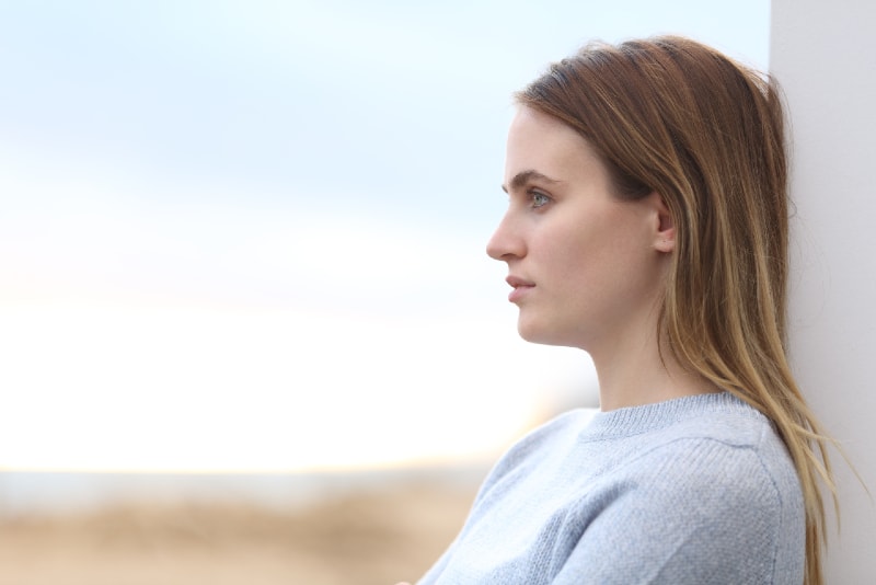 pensive woman in gray sweater leaning on wall outdoor